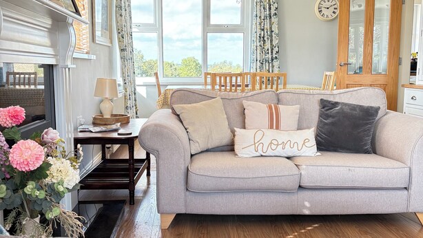 A cozy living room with a grey sofa, wooden floor, and a fireplace. - Peaceful Rural Retreat with Mountain Views - Benbradagh Country Cottage (Dungiven)
