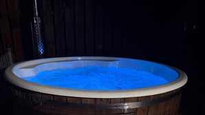 A wooden hot tub with a blue interior, surrounded by a wooden deck and a stone tile floor. - Peaceful Rural Retreat with Mountain Views - Benbradagh Country Cottage (Dungiven)