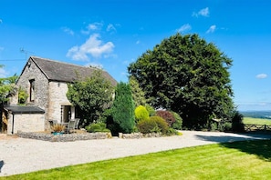 Situated in a lush landscape, this charming cottage offers a welcoming atmosphere with a small porch and outdoor seating.