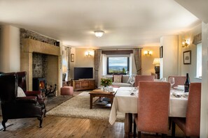 Cozy living room with a fireplace, sofa, armchairs, dining table for two, and a television, offering a scenic view.