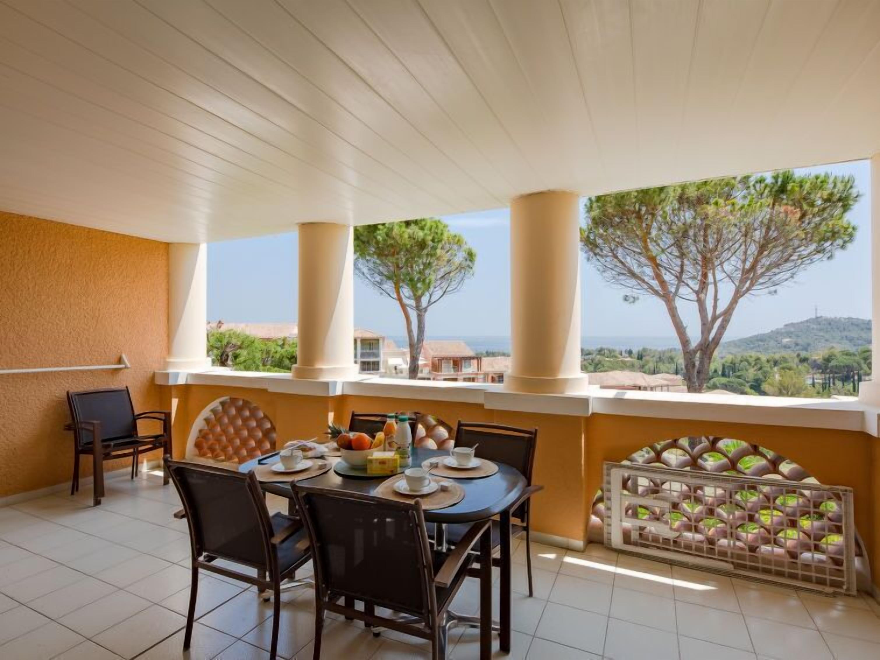 A covered outdoor dining area with a table set for two, chairs, and a view of the landscape.