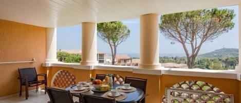 A covered outdoor dining area with a table set for two, chairs, and a view of the landscape.