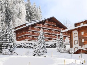 Un immeuble en bois à plusieurs étages, doté de balcons, entouré d’arbres couverts de neige.