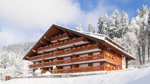 Eine Holzhütte mit mehreren Balkonen vor einer verschneiten Landschaft mit Bäumen.