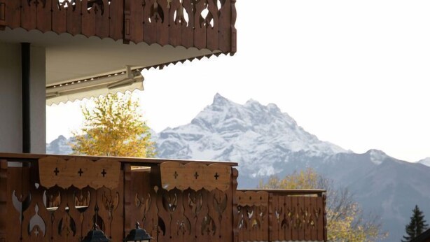 Ein Holzzaun mit aufwendigen Schnitzereien und einer Bergkulisse im Hintergrund.
