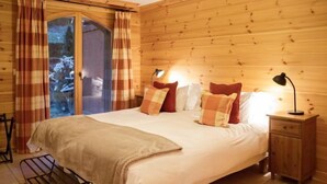Ein schlicht eingerichtetes Schlafzimmer mit Holzwänden, einem Bett, einem Nachttisch, einer Lampe und Blick durch eine Glastür.