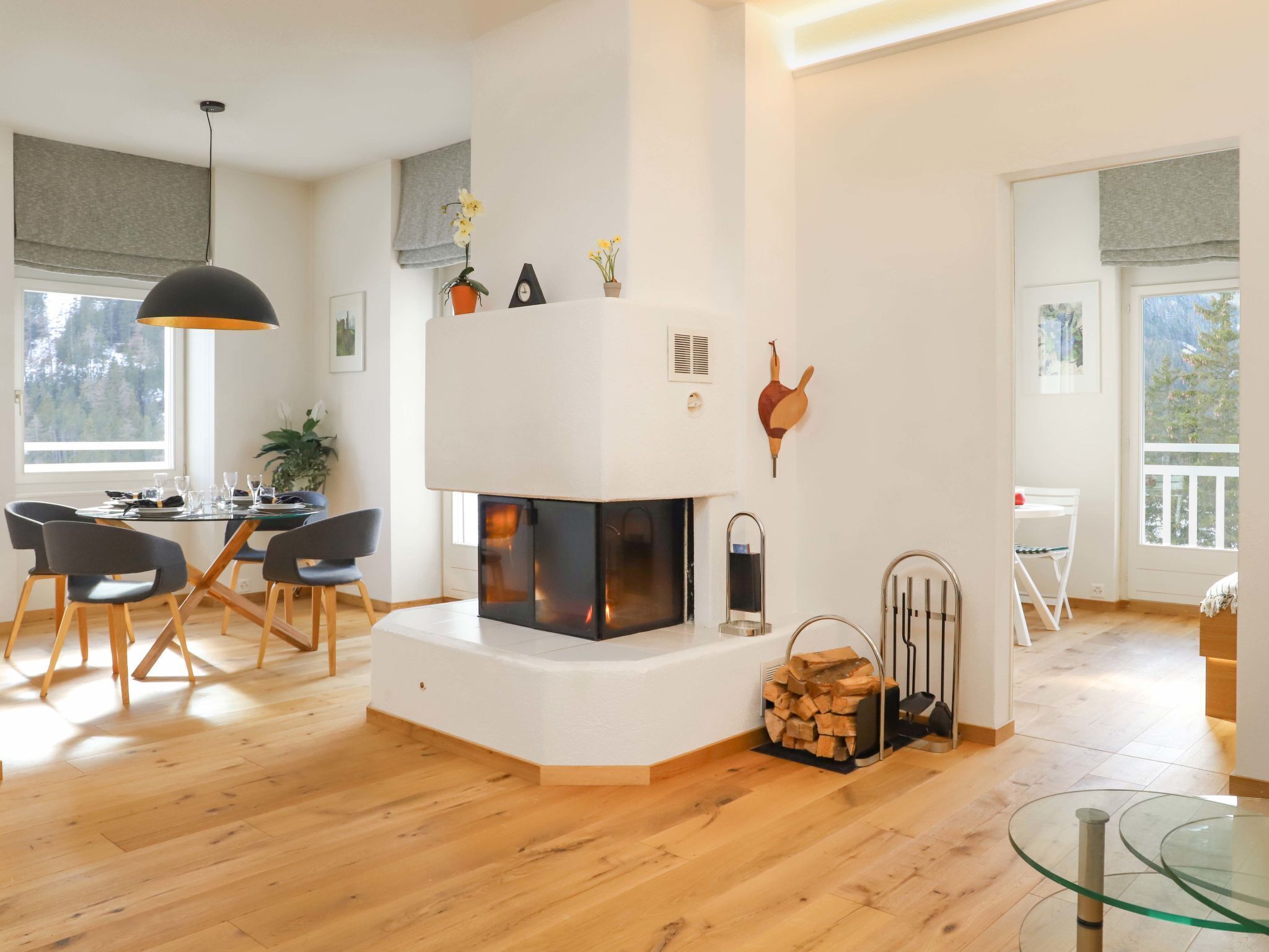 Ein modernes Wohnzimmer mit Kamin, Holzboden, einem Essbereich mit Stühlen und einem Glastisch.