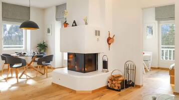 Ein modernes Wohnzimmer mit Kamin, Holzboden, einem Essbereich mit Stühlen und einem Glastisch.