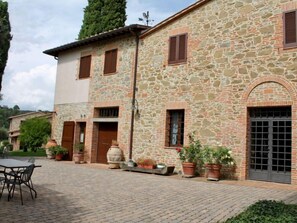 Un edificio de piedra con un patio central, que incluye una mesa grande y sillas, plantas en macetas y una veleta.