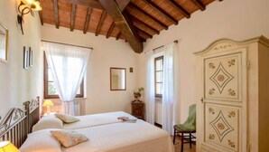A bedroom with a large bed, a wardrobe, a chair, and a window with curtains. - Casa Graziani by Interhome (Città della Pieve)