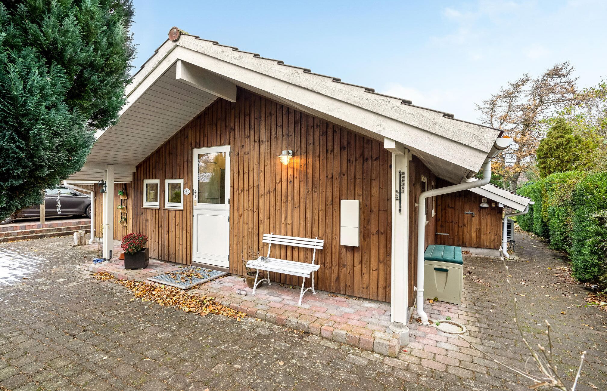 A wooden cabin with a sloped roof, a front door, a bench outside, and a small porch area.