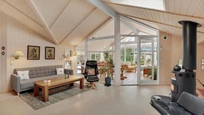 A spacious living room with a high ceiling, a fireplace, a sofa, a coffee table, and a view into the garden. - 2 bedroom amazing home in Slagelse (Slagelse)