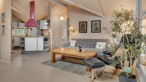A spacious living area with a wooden coffee table, a grey sofa, and black leather chairs. There is a kitchen visible in the background with white cabinets and a red pendant light. - 2 bedroom amazing home in Slagelse (Slagelse)