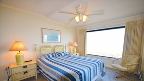 Ett hotellrum med en säng, sänglampor, en stol, en takfläkt och ett fönster med gardiner.