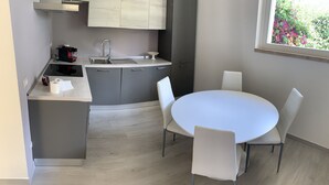 Une cuisine moderne avec des meubles gris, un évier en acier inoxydable et une table de salle à manger ronde entourée de chaises blanches.