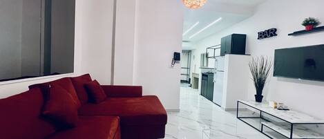 A modern living room with a red sofa, a marble floor, a TV mounted on the wall, and a kitchen area in the background.