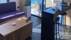 A modern living room with a sofa, a coffee table, and a dining area with a bar. Large windows offer a view of the sea. - Gondola marine resort (Halat)