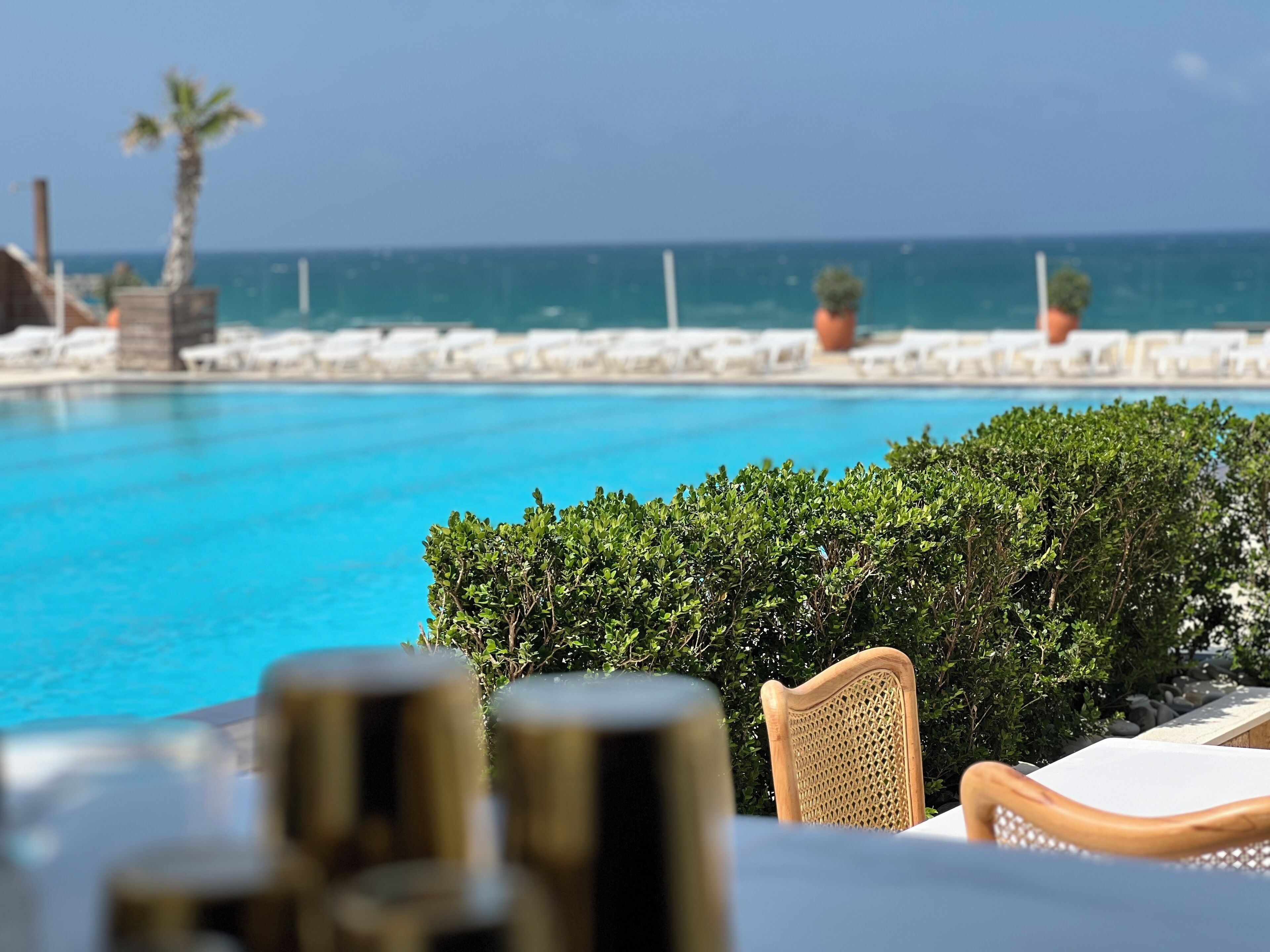 A poolside view with a clear view of the ocean, a chair, and a table.