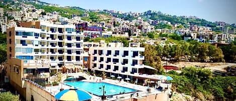 Un hotel de varios pisos, una piscina y vistas a una colina con edificios.