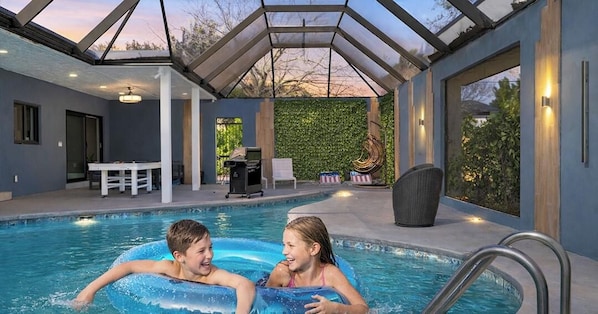 An indoor swimming pool with a glass ceiling, a table, chairs, and a wall with greenery. - South Miami Gem • Near Zoo, The Falls | Pool_BBQ (Cutler Bay)