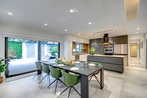A modern kitchen with a central island, built-in appliances, and a dining area with green chairs. - South Miami Gem • Near Zoo, The Falls | Pool_BBQ (Cutler Bay)