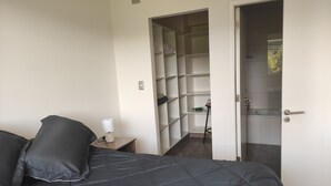 A bedroom with a bed, a bedside table with a lamp, a closet with shelves, and a bathroom door. - Buena Ubicación 2 Dormitorios 2 Baños (Puerto Montt)