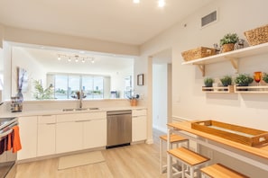 A modern kitchen with a dishwasher, wooden stools, and a view of the city.