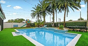 A swimming pool with a slide, palm trees, and a fenced area.