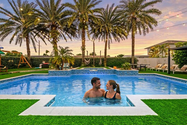 Una piscina con borde de azulejos, rodeada de césped y palmeras.