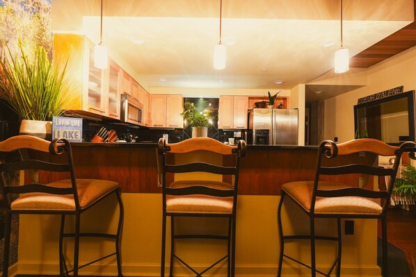 A modern kitchen with wooden cabinets, a central island with bar stools, and pendant lighting.
