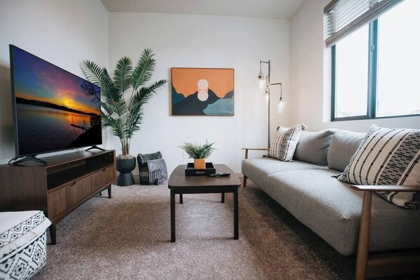 Ein modernes Wohnzimmer mit Flachbildfernseher, einer Couch, einem Couchtisch und zwei Blumentöpfen.