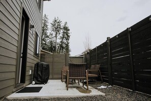 Ein Garten mit Grillhaus, zwei Korbstühlen und einer Holzterrasse.