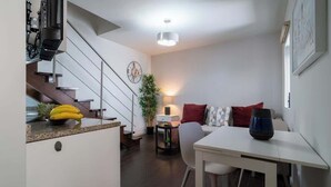 Cozinha moderna com área de refeições, escada e sala de estar com sofá e abajur.