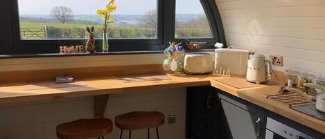 A kitchen with a large window, wooden stools, a toaster, and a kettle.