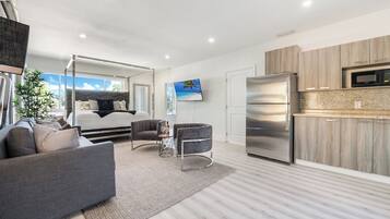 A modern living space with a sofa, a coffee table, a TV, a bed with a canopy, and a kitchen area with a refrigerator and microwave.