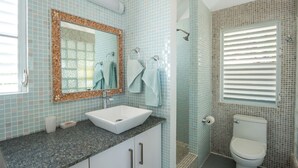 A bathroom with a white sink, a mirror with a decorative frame, a shower with a glass door, and a toilet. - Sea Breeze - An Intimate Villa Rental Overlooking Leverick Bay. (Virgin Gorda)