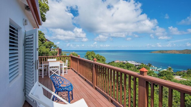 A wooden deck with a table and chairs, overlooking a coastal view with the sea and distant land. - Sea Breeze - An Intimate Villa Rental Overlooking Leverick Bay. (Virgin Gorda)
