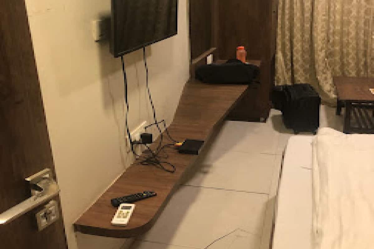 A hotel room with a bed, a TV mounted on the wall, a small table, and a suitcase.