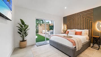 Un dormitorio con cama, planta en maceta, puerta corrediza de vidrio a un balcón y lámpara fijada a la pared.
