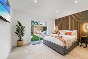 Une chambre à coucher avec un lit, une plante en pot, une porte-fenêtre coulissante donnant sur un balcon et un luminaire fixé au mur.