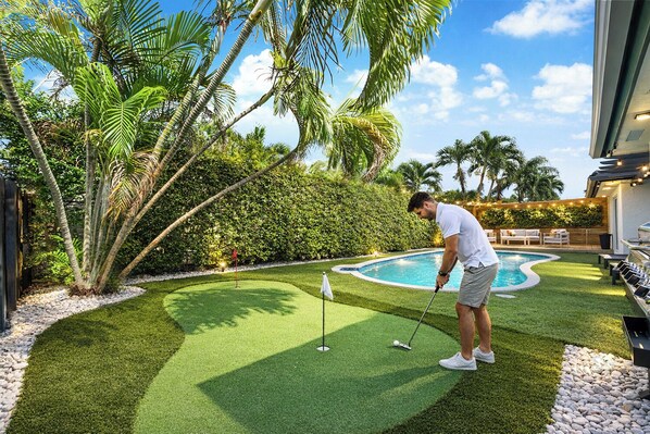 Un homme jouant au golf sur un terrain verdoyant, avec une piscine en arrière-plan.