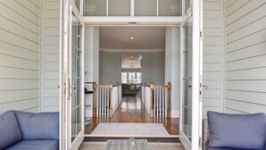 A hallway with a glass door leading to a dining area, a wooden floor, and a blue sofa on the left. - 5 Sandy Beach Trail- Beach House w/ Private Pool (Hilton Head)