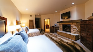 A hotel room with two beds, a fireplace, a TV mounted on the wall, and a wooden cabinet.
