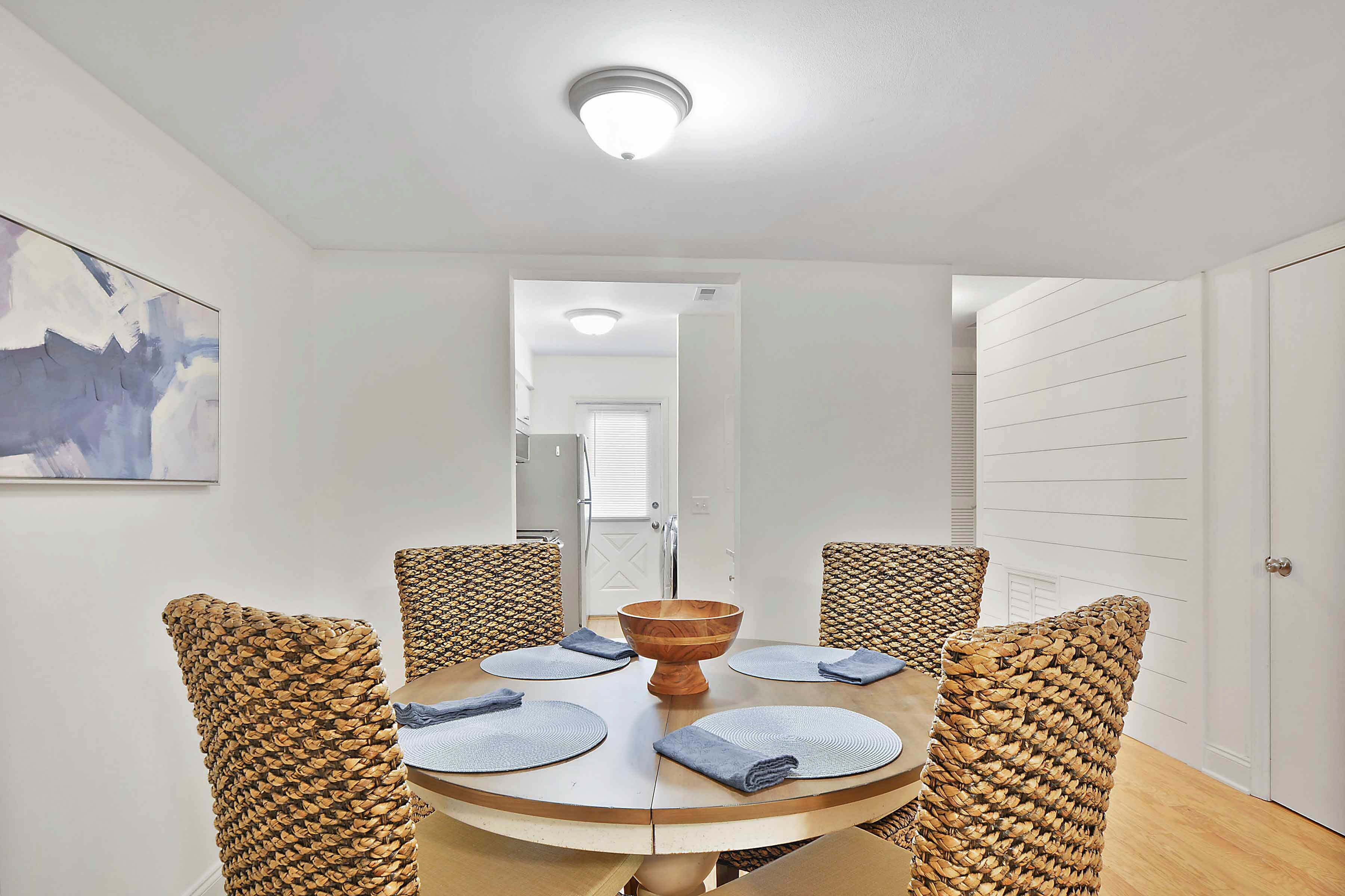 A dining area with a round table, a central wooden bowl, and woven chairs.