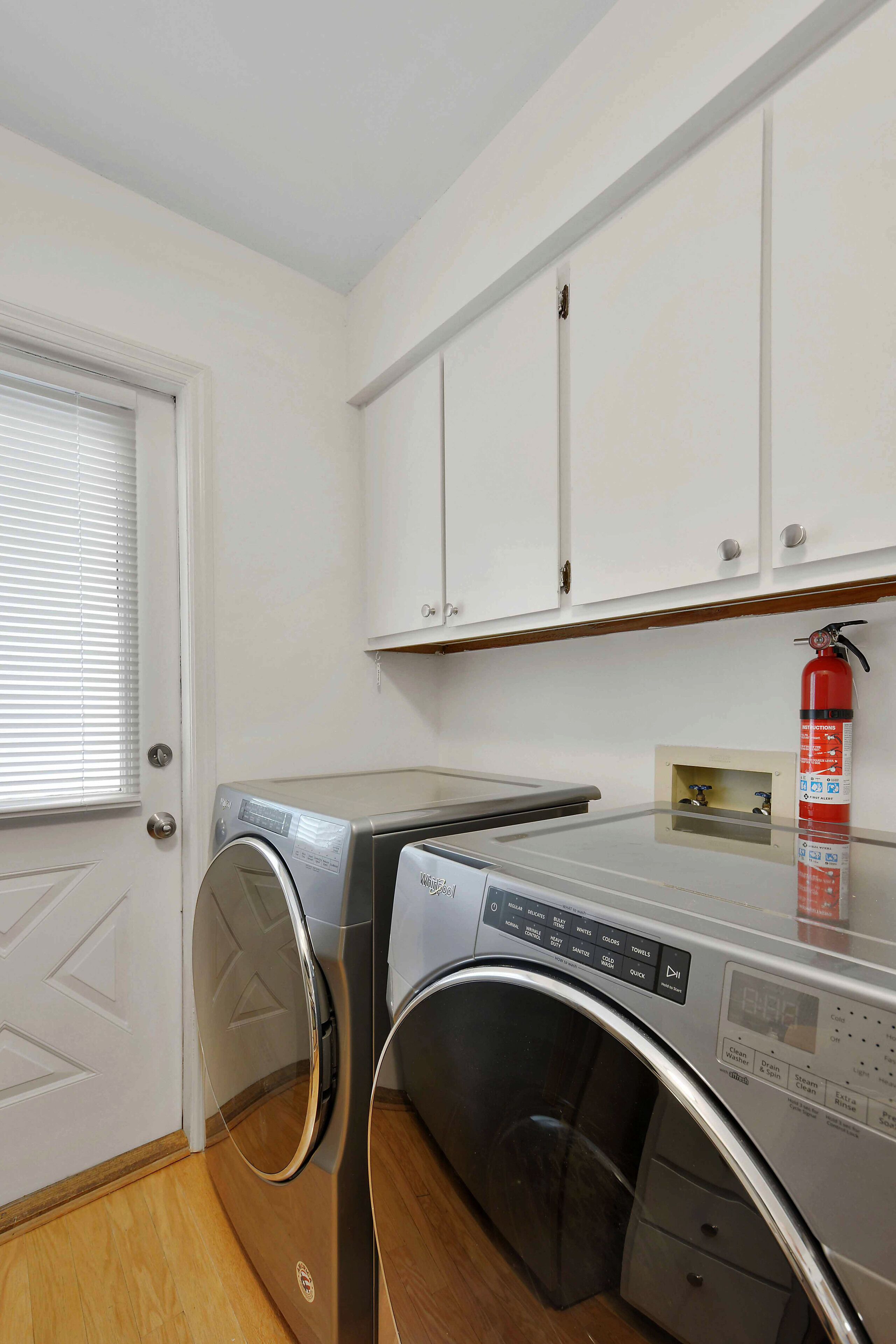 A laundry room with a front-loading washing machine, a dryer, and a fire extinguisher on the wall.