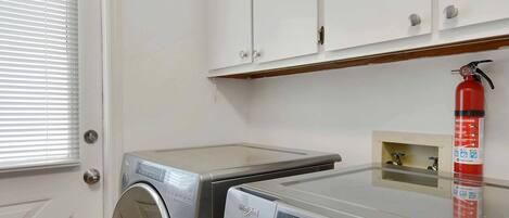 A laundry room with a front-loading washing machine, a dryer, and a fire extinguisher on the wall.