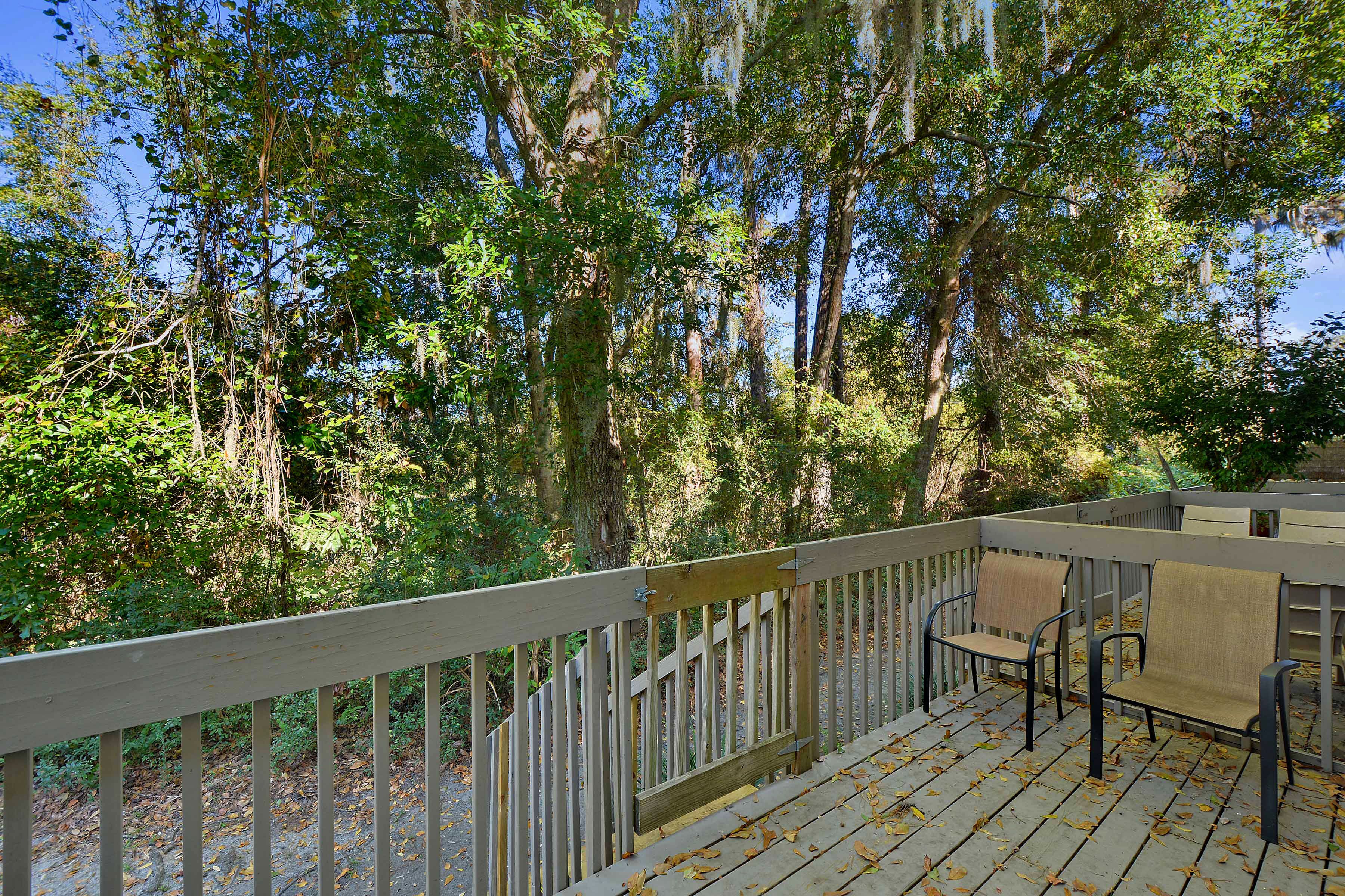 A wooden deck with two chairs and a bench, surrounded by trees.