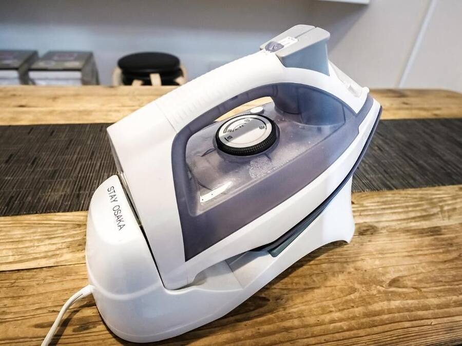 A white iron with a control dial and a cord plugged in, placed on a wooden surface.
