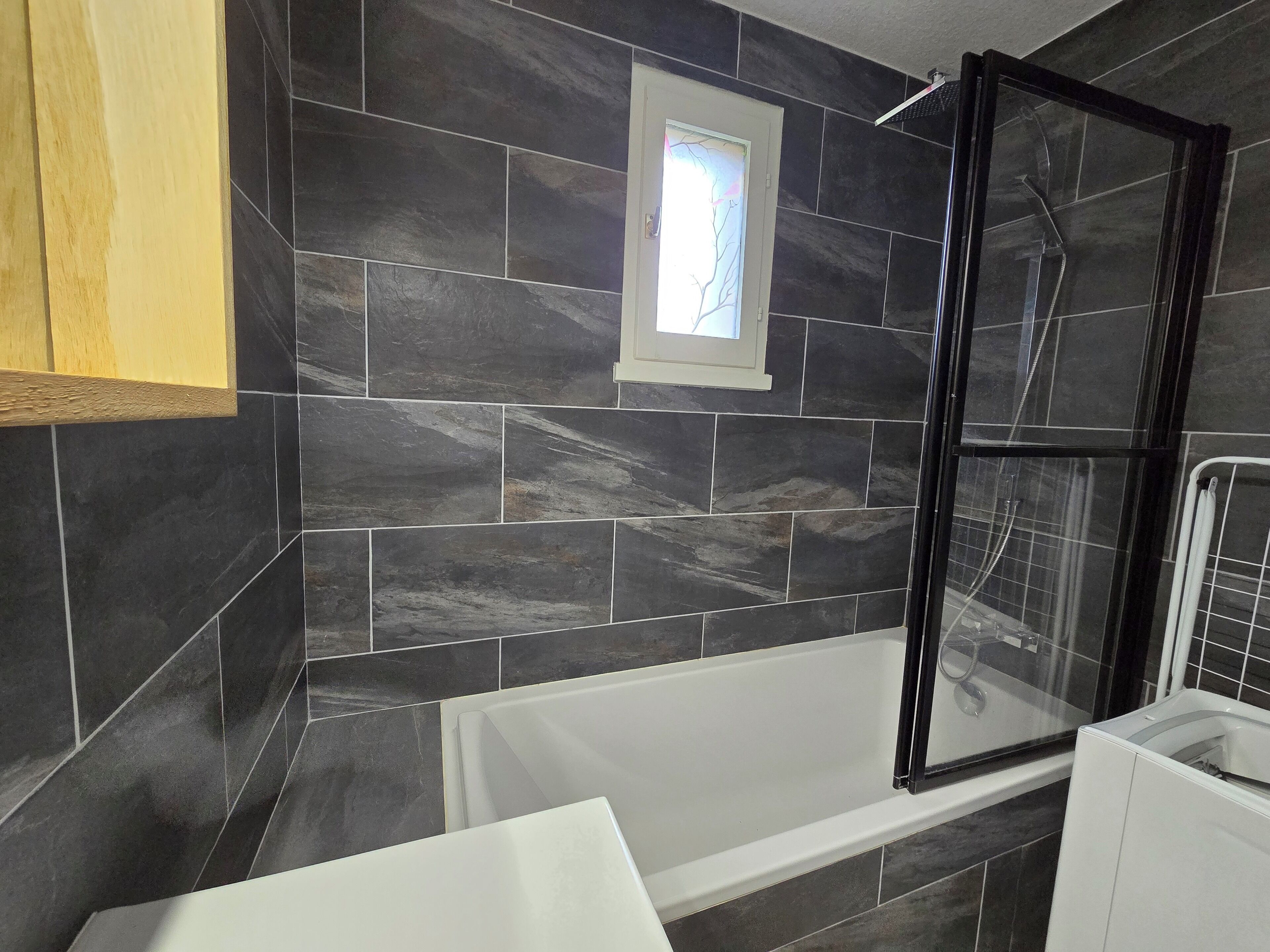 Une salle de bain moderne avec des carreaux de pierre foncée, une douche à parois de verre et une baignoire blanche.