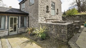 A stone building with a sloped roof, a door with glass panels, and potted plants in the foreground. - The Dovecote (Denbigh)